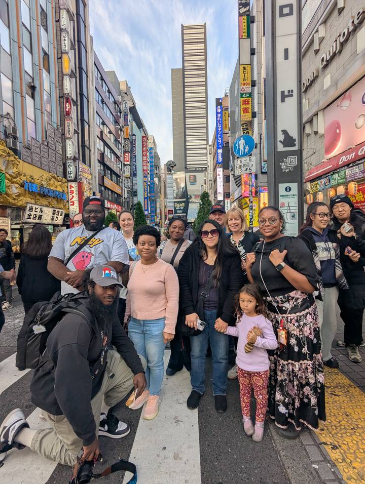 Tour group poses on a busy neon-lit street in Shinjuku with colorful signs towering behind.