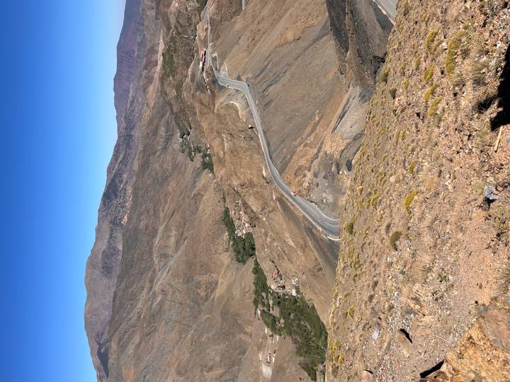 Snaking mountain road descends through barren brown slopes toward small villages in a rugged valley.