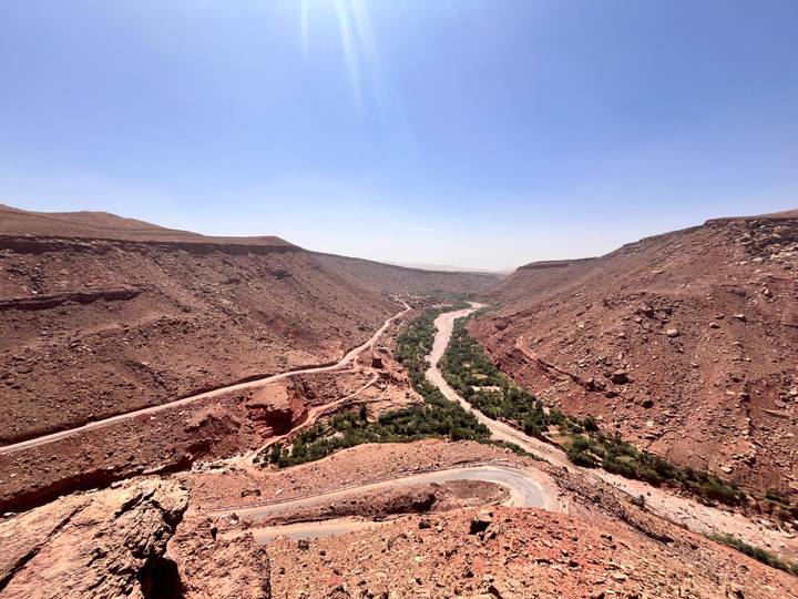 Wide canyon with winding river and rugged red cliffs stretching into hazy horizon.