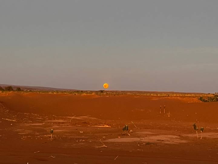 Large orange moon rises over a flat, empty desert landscape at dusk.