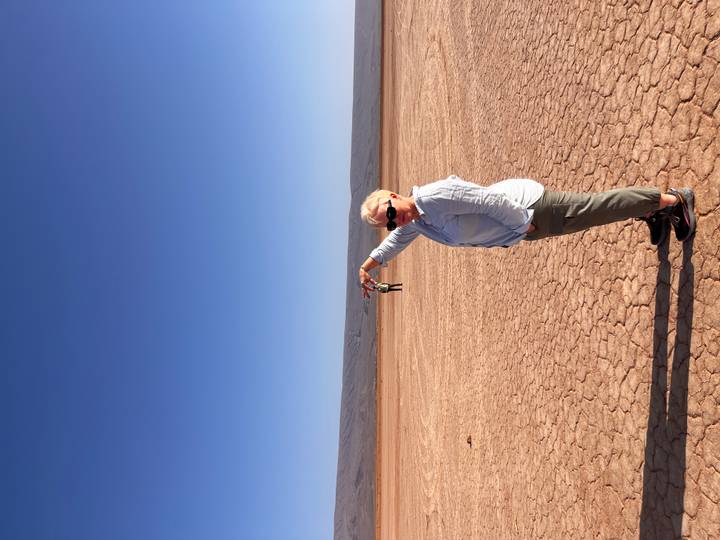 Woman poses with outstretched arm creating a forced-perspective illusion on a cracked desert lakebed.