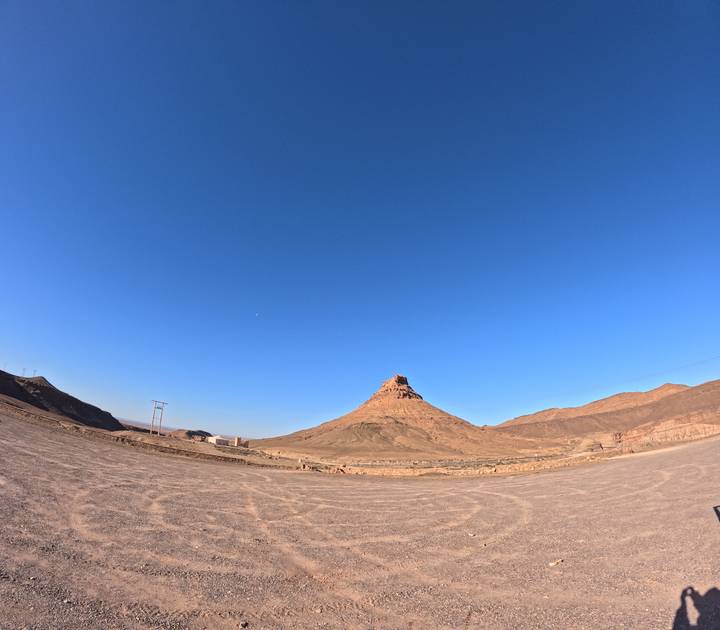 Isolated conical mountain rises from a vast flat desert plain beneath a deep blue sky.