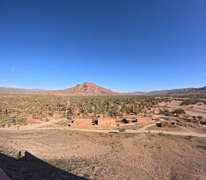 Green palm grove spreads across valley floor beneath a rugged flat-topped mountain.