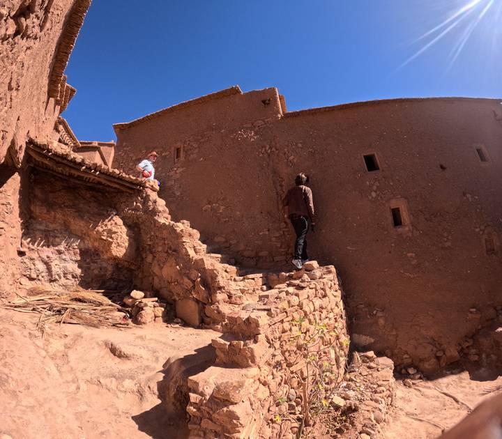 Travelers climb stone steps of an earthen kasbah, studying its ancient walls.