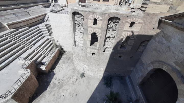 Aerial view down into ancient stone amphitheater walls and stepped seating partly in shadow.