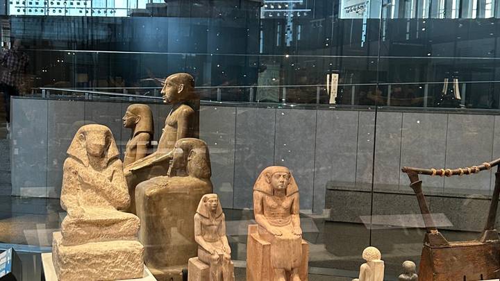 Glass-cased display of ancient Egyptian statues and artifacts inside a modern museum gallery.