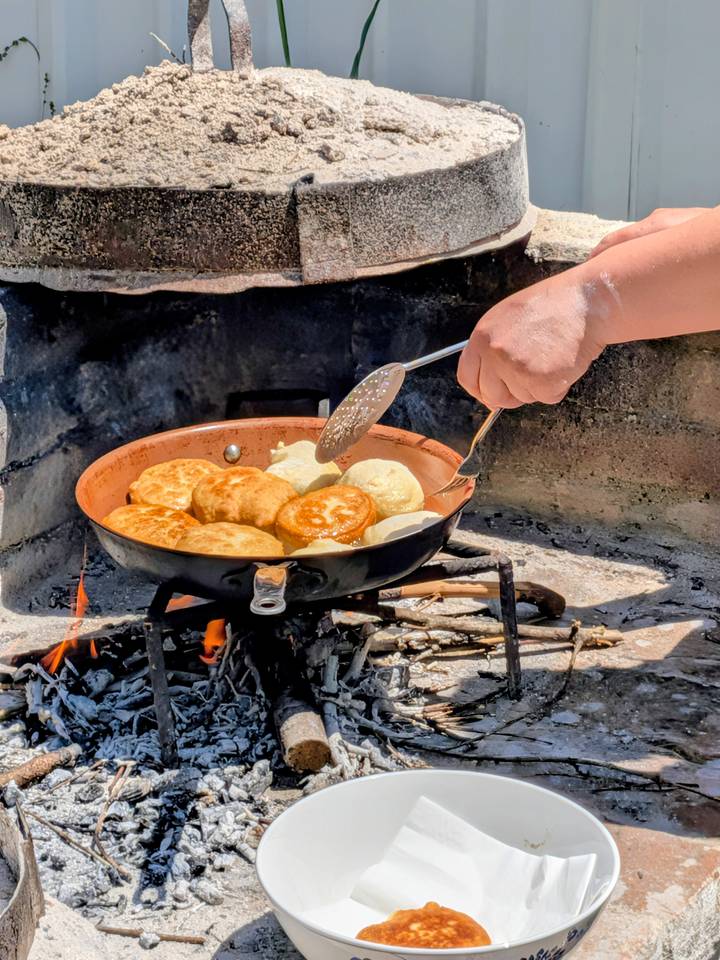 Golden dough pieces fry in a copper pan over an open wood fire during a traditional cooking session.