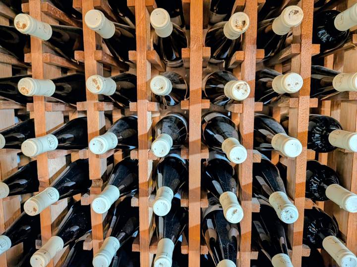 Rows of wine bottles are stacked horizontally in a wooden rack inside a cellar.