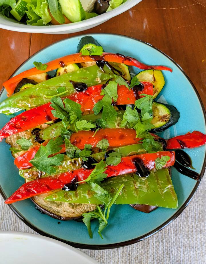 Colorful grilled peppers and zucchini drizzled with balsamic glaze are garnished with fresh parsley.