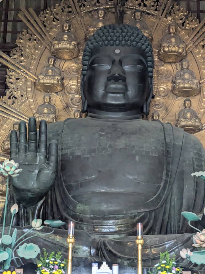 The massive bronze Buddha statue raises a hand in blessing against an ornate golden backdrop.