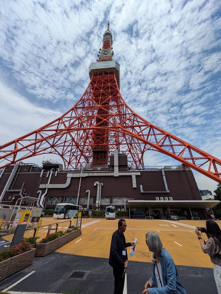 A bold low-angle view of the bright orange Tokyo Tower steel framework against a blue sky.