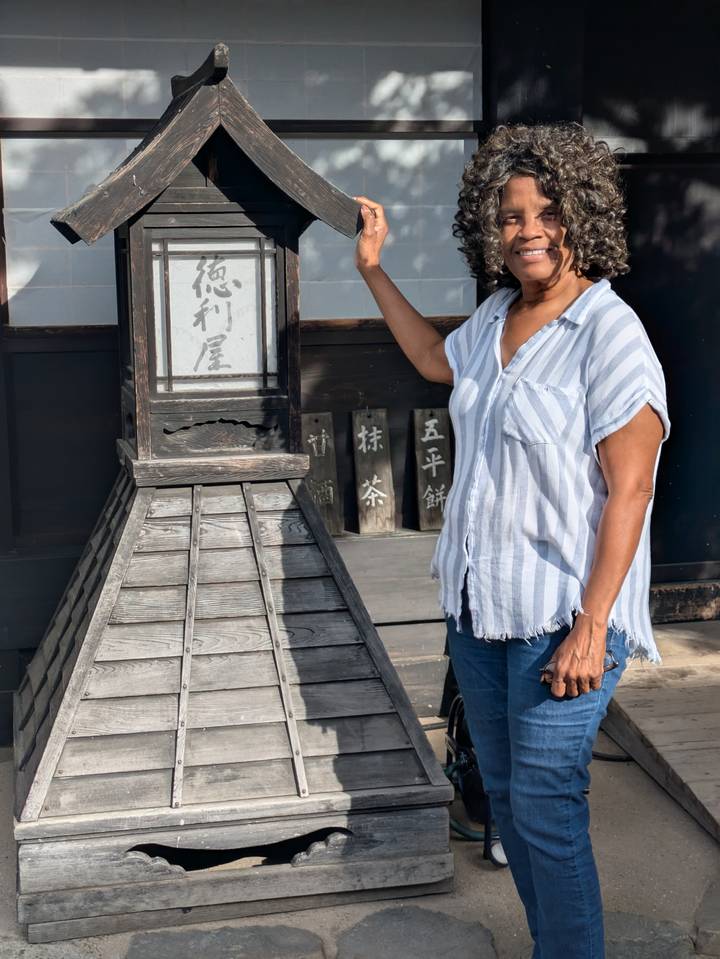 A traveler poses beside a traditional wooden signboard outside a historic building.