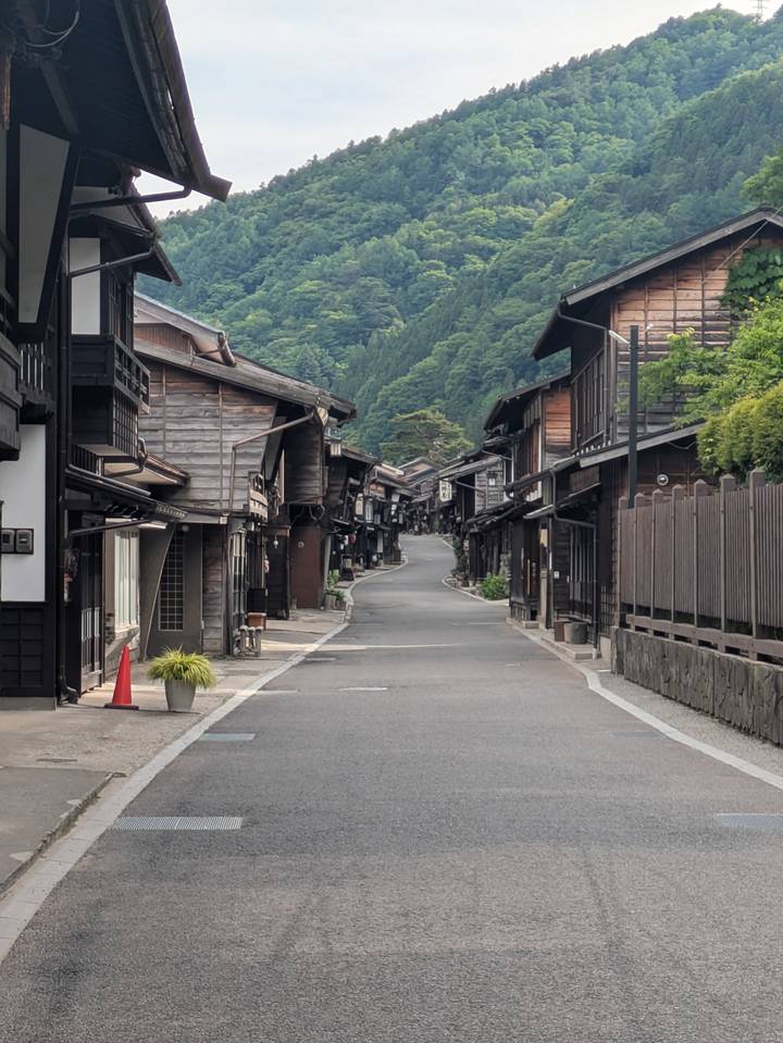 A quiet Edo-period wooden street curves uphill through a mountain village lined with dark timber houses.