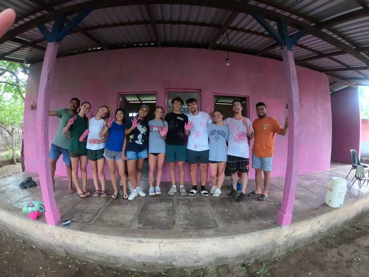 Smiling volunteers pose in front of a newly painted bright-pink rural building