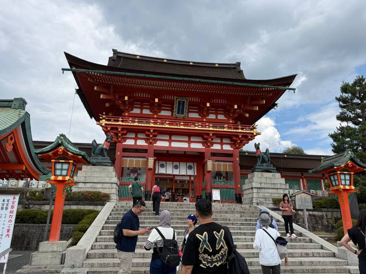 Grand vermilion shrine gate guarded by fox statues with tourists gathered on the steps.