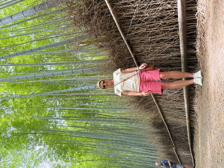 Visitor smiles beneath towering emerald bamboo stalks along a forest path.