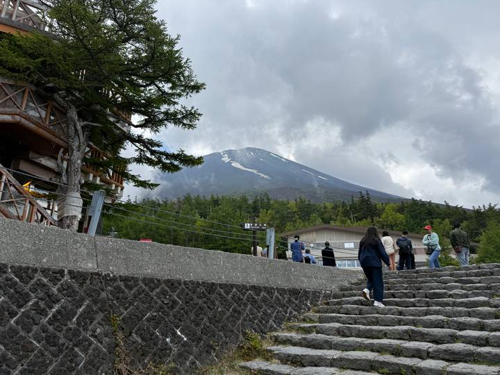 Hikers ascend stone steps toward a viewpoint with snow-streaked Mount Fuji looming beyond.