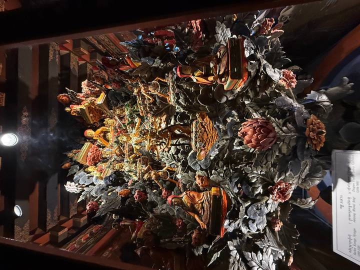 Intricately carved multi-figure Buddhist diorama displayed inside a dimly lit museum case