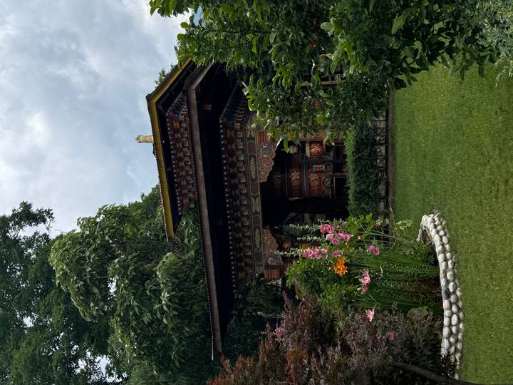 Colourful Bhutanese prayer wheel pavilion surrounded by lush garden and flowers