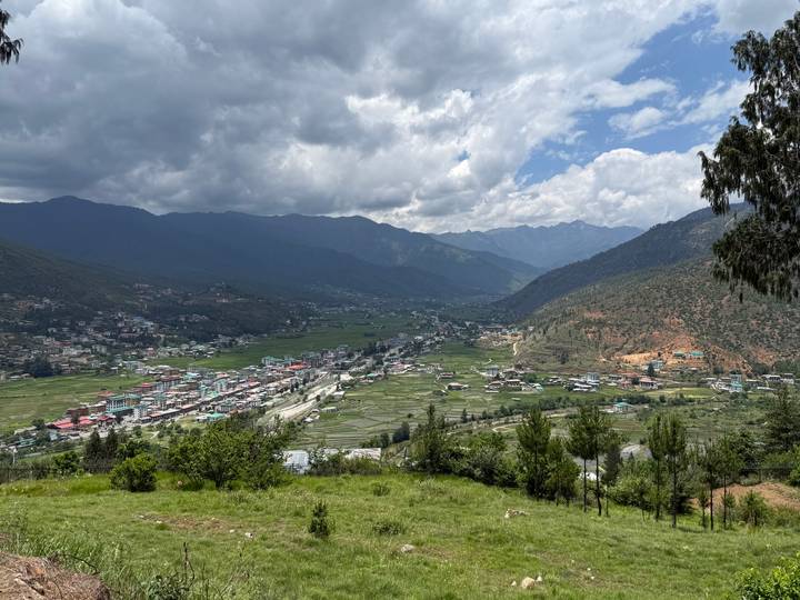Panoramic view of a Bhutanese valley town surrounded by mountain ranges under dramatic clouds