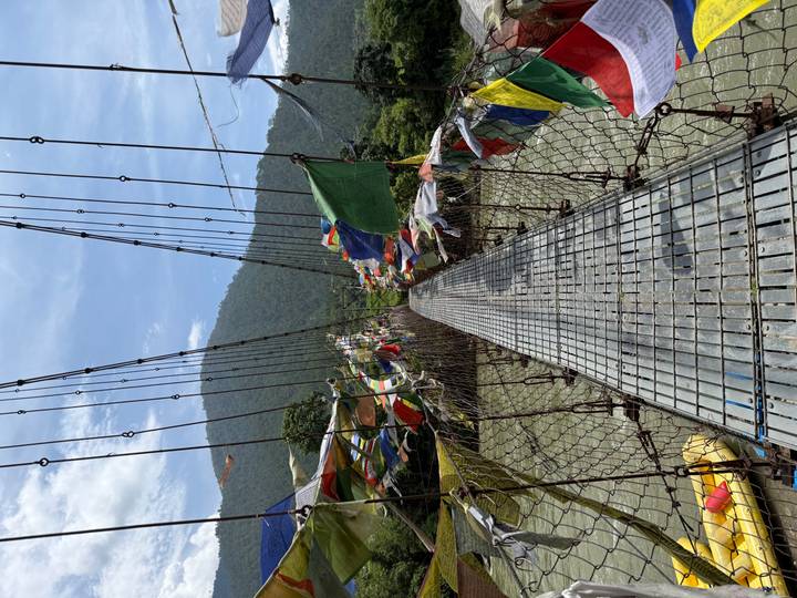Narrow wire suspension bridge covered with multicolored prayer flags spanning a fast river
