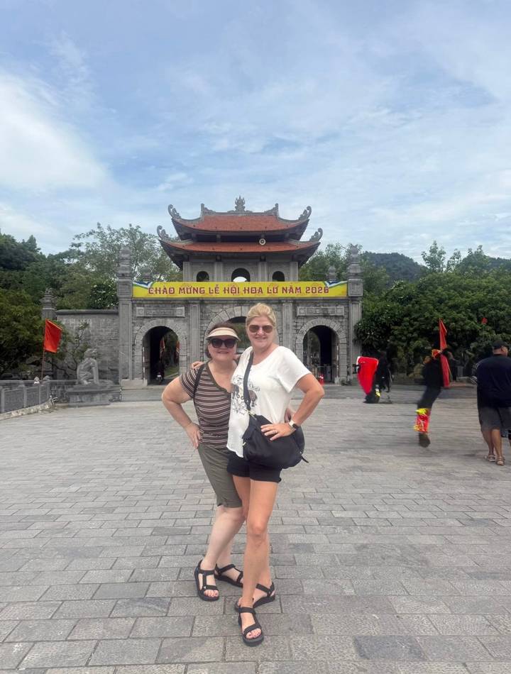 Two women posing in front of the ancient stone gate of Hoa Lu with festival banner overhead.