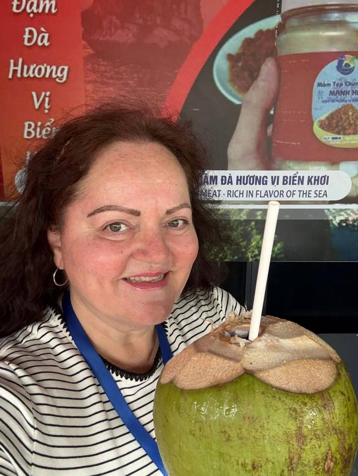 Close-up of a woman smiling while sipping fresh coconut through a straw.