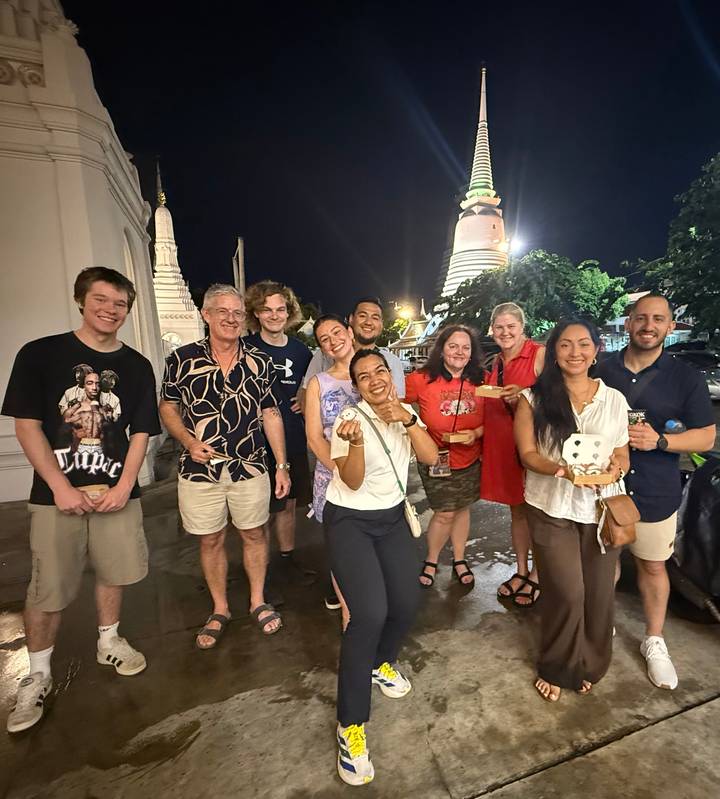 Nighttime street food tour group smiling and holding treats with a brightly lit stupa in background.