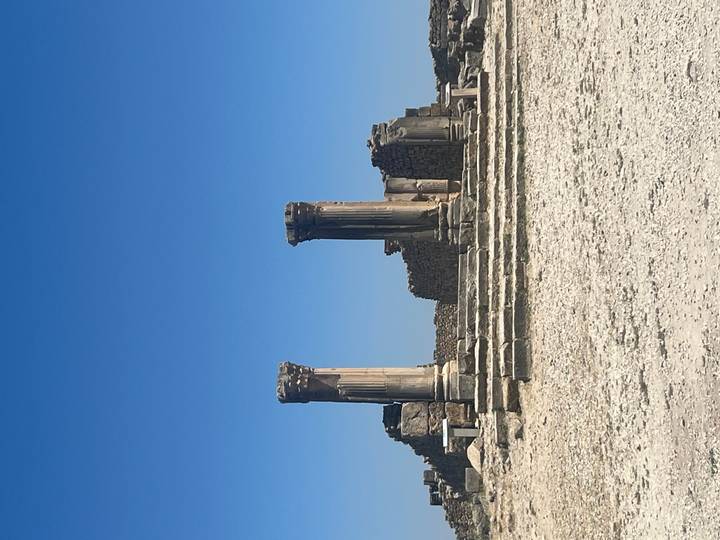Two standing Roman columns and scattered ruins under a clear blue sky.