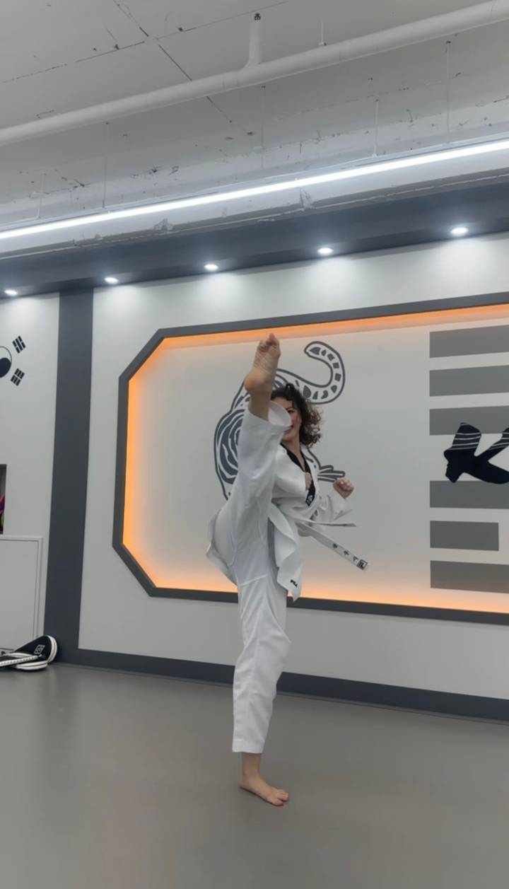Martial artist performs a high kick in a modern dojang with illuminated wall design.