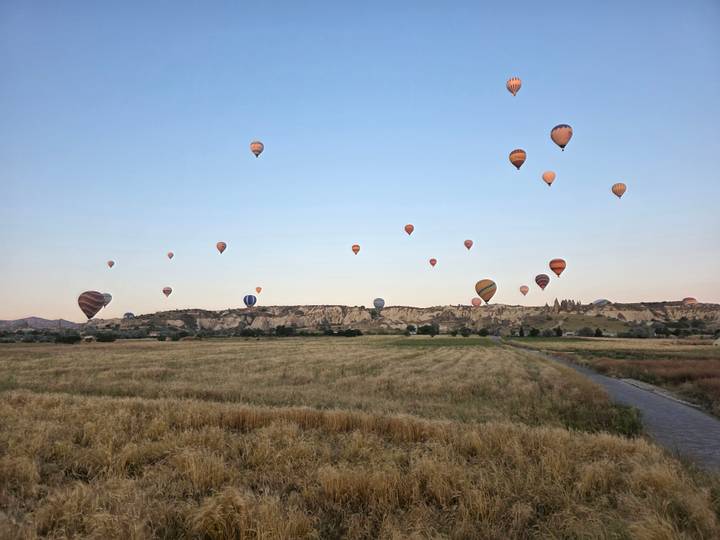 Dozens of colorful hot-air balloons rising over Cappadocia’s rocky landscape at dawn.