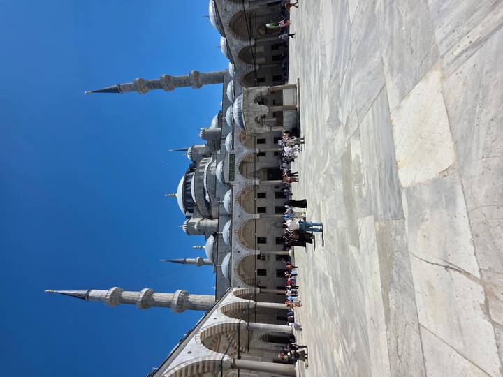 Courtyard view of the Blue Mosque with multiple minarets under clear blue sky.