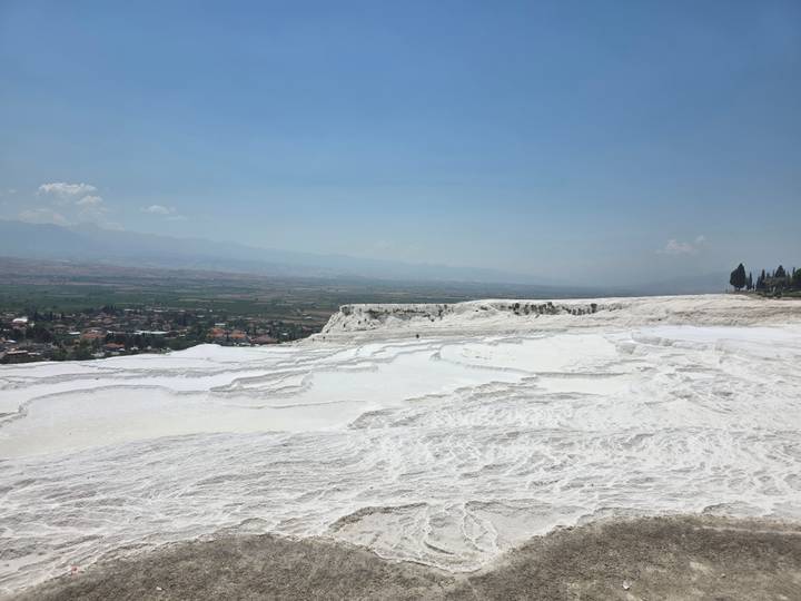 White travertine terraces of Pamukkale overlooking vast plain under blue sky.
