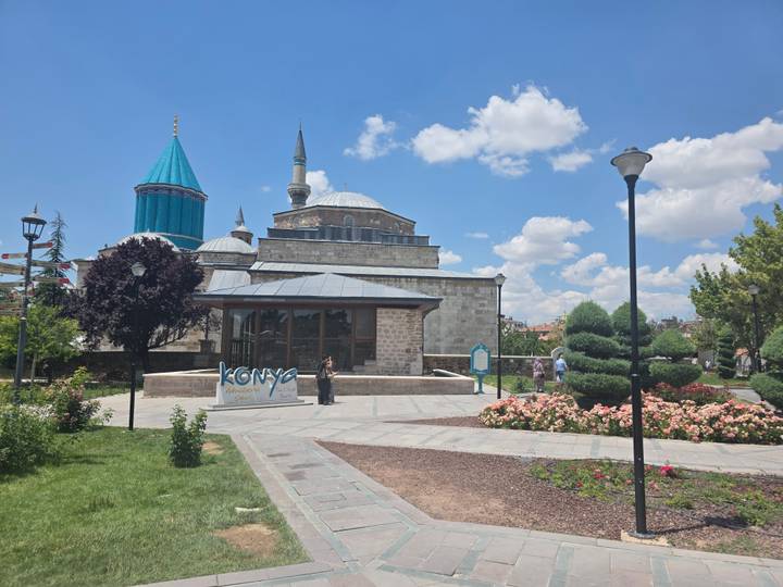 Exterior of Mevlana Museum complex in Konya with gardens, flowers and turquoise dome.