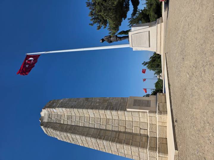 Gallipoli memorial with Turkish flags and soldier statue under clear sky.