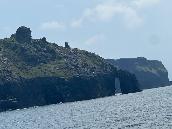 Rocky sea cliffs with a natural arch jutting into blue water under a sunny sky