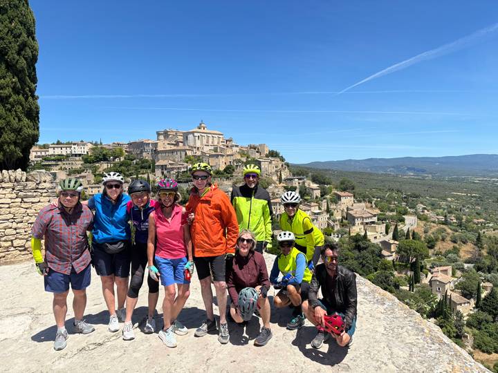 Cycling group posing on a viewpoint overlooking the hilltop village of Gordes in Provence.