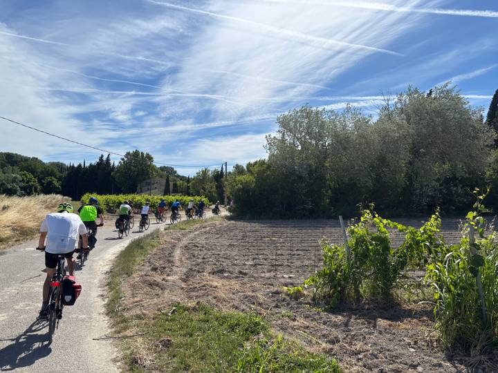 Long line of cyclists riding through rural farmland under a streaked blue sky.
