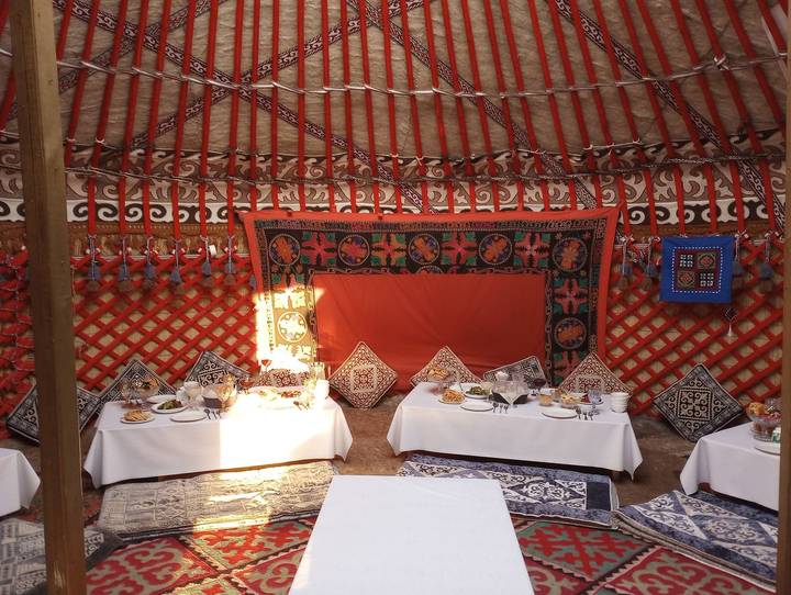 Interior of traditional Kyrgyz yurt set for communal meal with patterned felt decorations and low tables