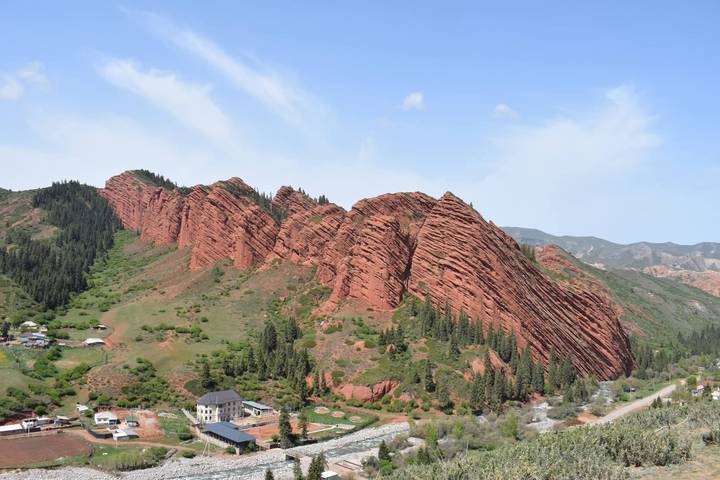 Jagged red sandstone ridges of Jeti-Ögüz Valley framed by green forest and village below