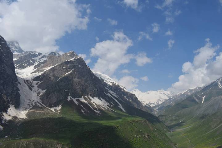 Snow-capped peaks and green valley of Fann Mountains beneath scattered clouds