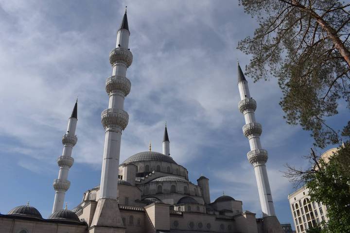 Grand white mosque with four tall minarets against blue sky in Ashgabat