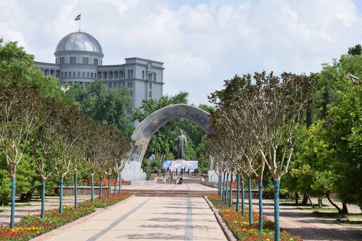 City park in Dushanbe with curved monument arch, fountains and government buildings beyond