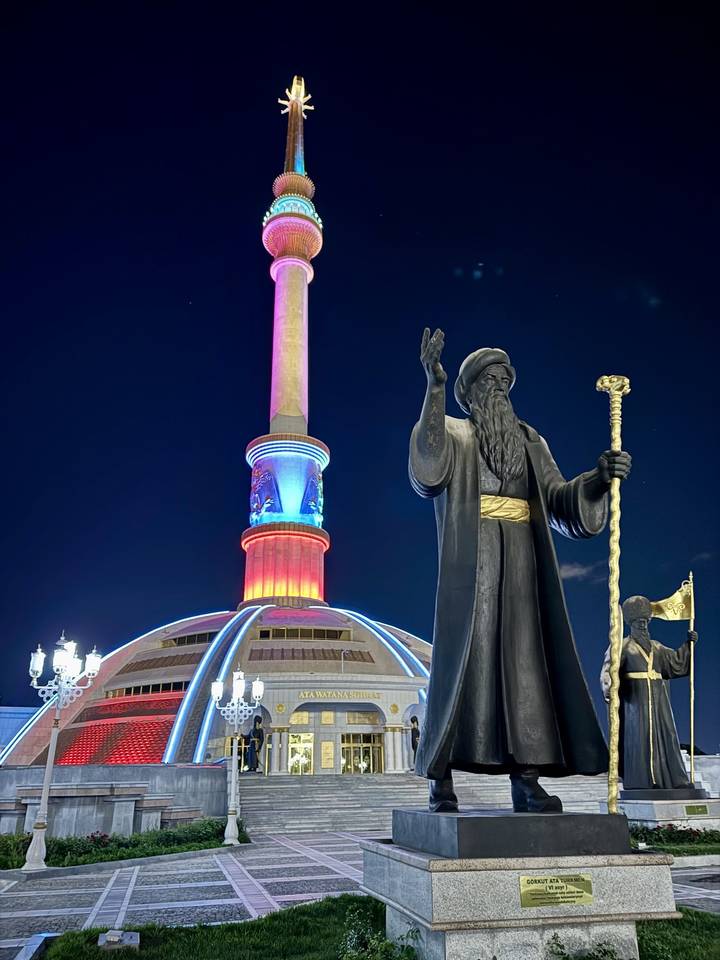 Nighttime monument with colourful LED lighting and large statue in front