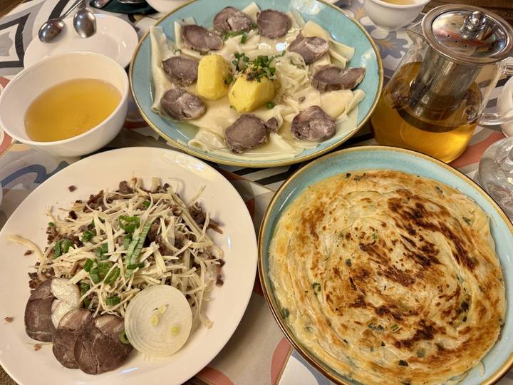 Table filled with Central Asian dishes including noodles, broth, and flatbread