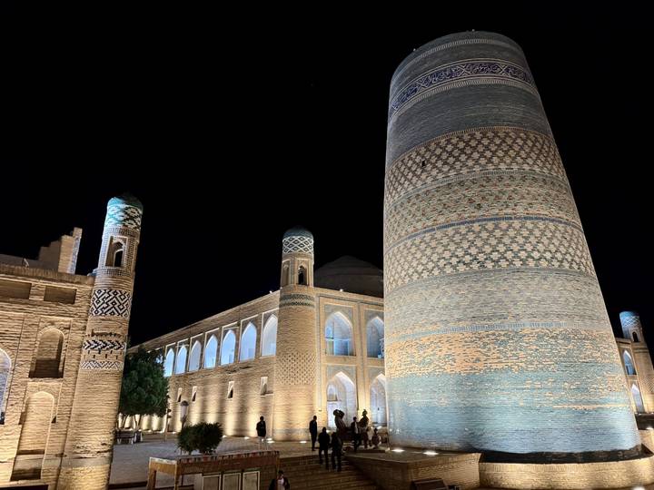 Historic madrasah and tall patterned minaret lit warmly against dark sky