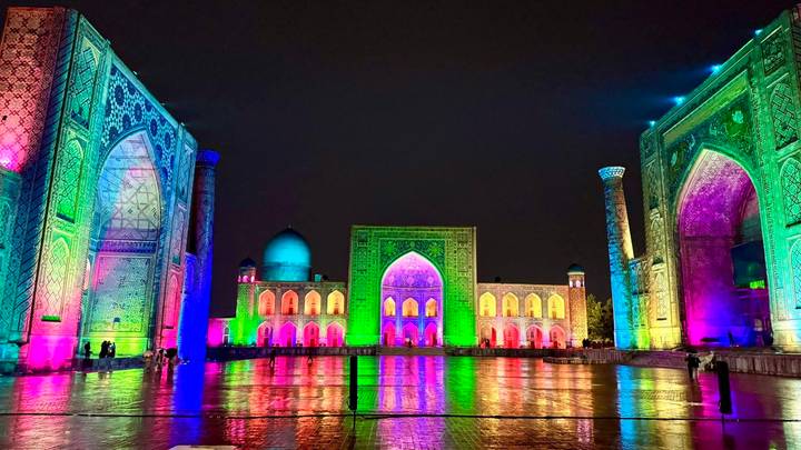 Registan Square in Samarkand glowing with multicolour lights reflected on wet pavement at night