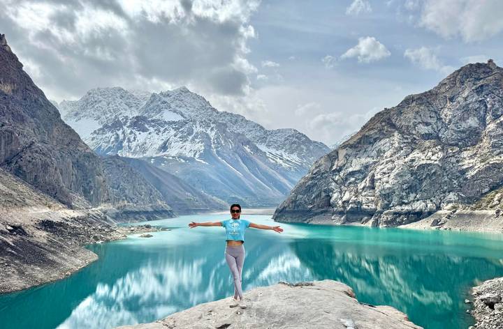 Traveller with arms wide open standing above turquoise alpine lake ringed by snowy peaks