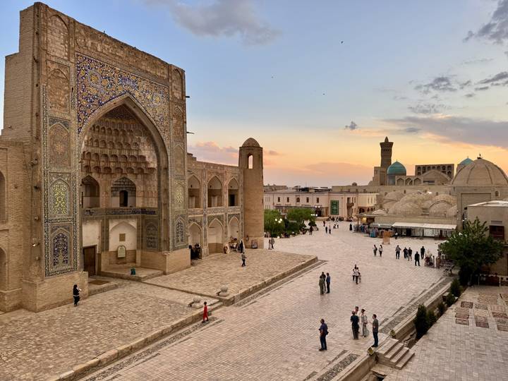 Bukhara’s historic square at golden hour with tourists walking under orange sky