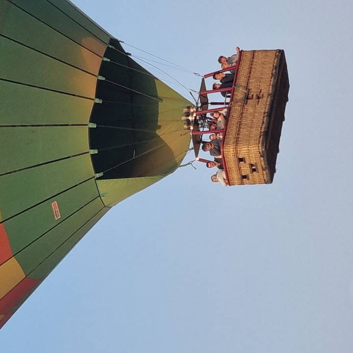 Hot-air balloon basket with passengers smiling during a flight against a clear morning sky.
